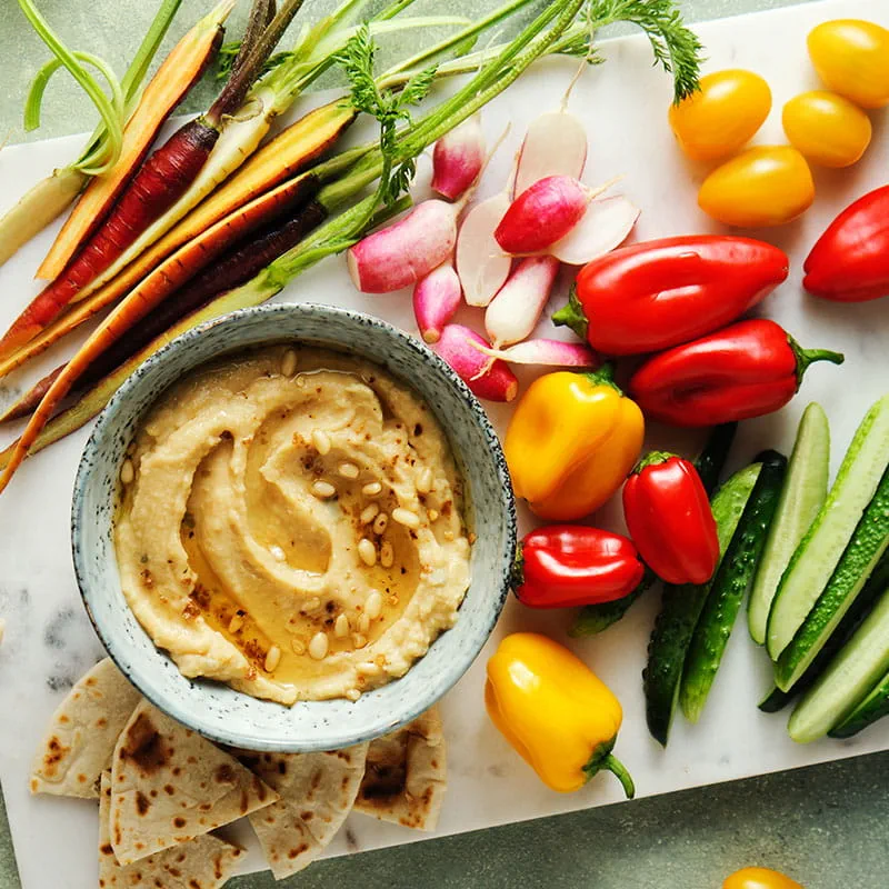 Huisgemaakte hummus met kruiden, pijnboompitten en groenteschotel met regenboog